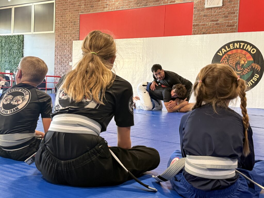 Students practicing Jiu-Jitsu techniques during a class on grey mats.